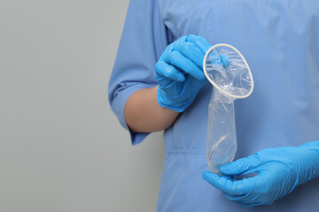 Doctor with unrolled female condom on light grey background, closeup. Space for text