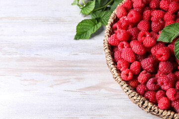 Tasty ripe raspberries and green leaves on white wooden table, space for text