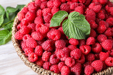 Tasty ripe raspberries and green leaves on white table, closeup