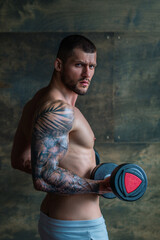 Fototapeta na wymiar Sexy naked body. Sexy muscular man pumps his muscles and lifts dumbbells in gym. Strong fit man exercising with dumbbells. Muscular young handsome man lifting weights