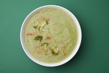 Delicious broccoli cream soup on green background, top view