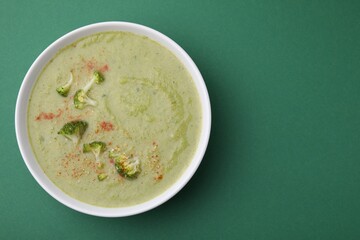 Delicious broccoli cream soup on green background, top view. Space for text