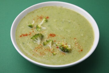 Delicious broccoli cream soup on green background, closeup