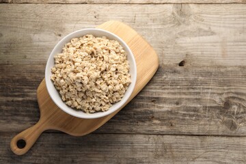 Tasty boiled oatmeal in bowl on wooden table, top view. Space for text
