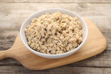 Tasty boiled oatmeal in bowl on wooden table, closeup