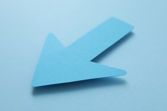 One paper arrow on light blue background, closeup