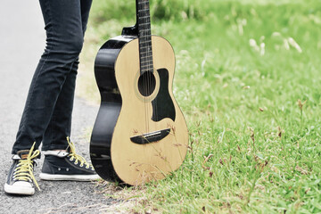 acoustic guitar and feet standing on green grass - obrazy, fototapety, plakaty