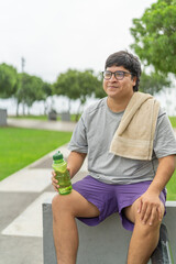 Overweight man sitting on a park drinking water after exercise