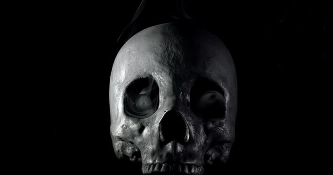 Smoke slowly creeping through the eye sockets of a terrifying human skull, haunted spirt, or frightening ghost for Halloween or other spooky scene.