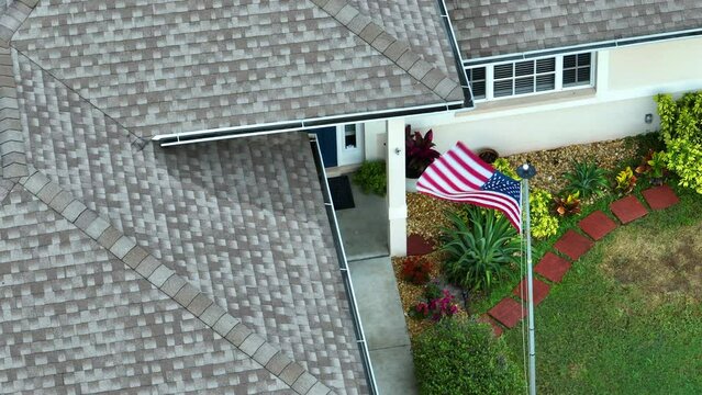 Florida suburban home with USA national flag waving on wind in front yard. American stars and stripes spangled banner as symbol of democracy