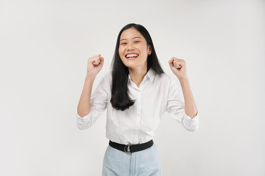 Photo of a young woman 20s  clenching fists, wearing a white shirt, and isolated on a white background.