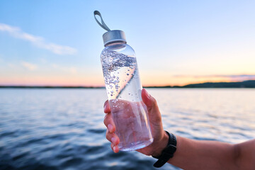 A man holds a bottle of water against the backdrop of a lake.
