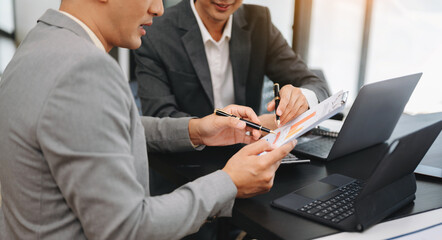Business documents on office table with smart phone and laptop and two colleagues discussing data...