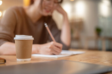 Fototapeta na wymiar Close-up image of a girl keeping her diary in a coffee shop, selective focus at a coffee cup.