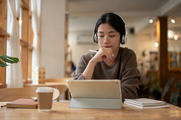 A focused woman using her tablet, studying online, or having an online meeting in a cafe.