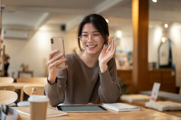 A woman enjoys talking on a video call with her friends while sitting at a table in a coffee shop.