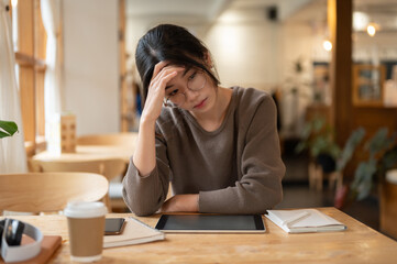 A stressed Asian woman is concerned about her project's deadline while working remotely at a cafe.