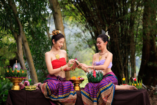 young woman in ancient thai dress helps each other to make krathong.