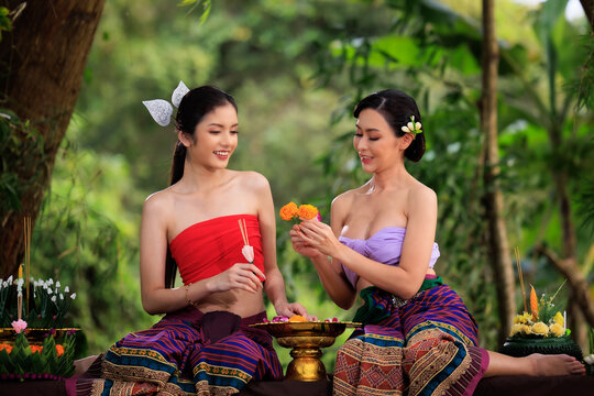 young woman in ancient thai dress helps each other to make krathong.