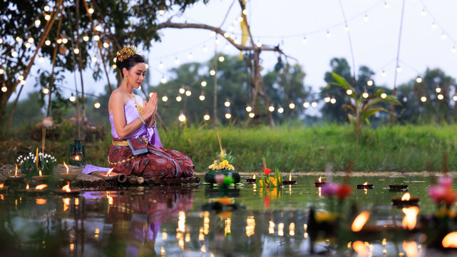 Loi Krathong Festival, Thai woman holding hand pay respect sitting on a raft by the river, Asian women in traditional Thai costumes bring krathongs to float on Loi Krathong Day,