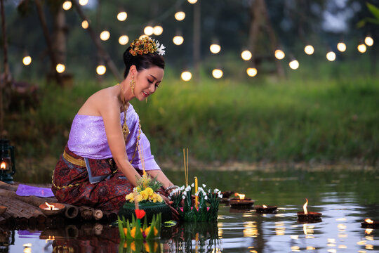Loi Krathong Festival, Thai woman holding a krathong sitting on a raft by the river, Asian women in traditional Thai costumes bring krathongs to float on Loi Krathong Day,