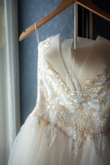 A tulle and lace wedding dress hanging from a wooden hanger over a fabric screen