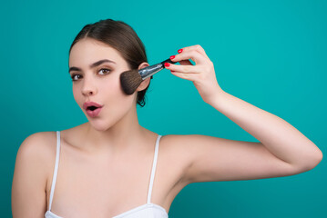 Woman hold blush blusher apply powder visage isolated over studio background. Girl powdering cheeks. Makeup brush. Female model gets blush powder on the cheekbones.