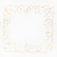 Square Christmas lights wire garland border and golden stars confetti over white background. Flat lay, copy space.