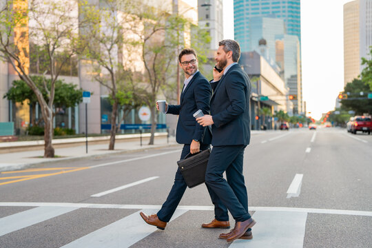 Two attractive confident hispanic businessmen in suits walking outdoors at the city streets. Two businessmen walking and talking at urban city. Middle eastern businessman walking near office building.
