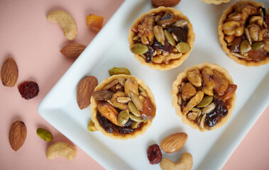Appetizing tartlets stuffed with hazelnuts walnuts covered with a layer of liquid caramel. Homemade mini tart, selective focus. Top view with nuts as background.