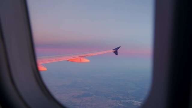 Aircraft Wing of flying above clouds airplane as seen by passenger through porthole on sunset. Wide footage 