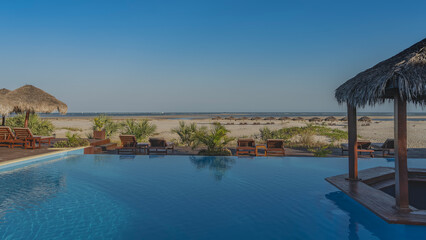 Recreation area on the ocean. Sunbeds and straw sun umbrellas stand next to the blue swimming pool. In the distance you can see the sandy beach, the waves of the Mozambique Channel. Madagascar. 