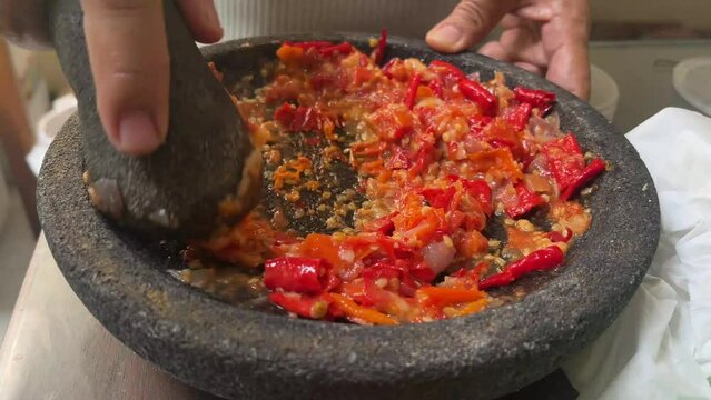 Sambal bawang in the making using traditional tool called ulekan. Sambal bawang is a delicious traditional sauce from Indonesia made from chilies and garlic.