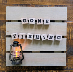 "Gone Fishing" spelled out with wooden letters and a miniature lantern placed on a wooden sign board.