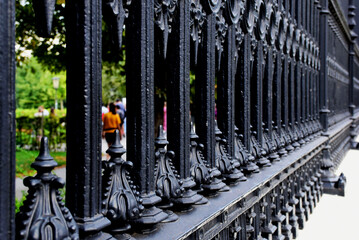 heavy black cast iron fence. strong diminishing perspective view. sidewalk detail. people and green...