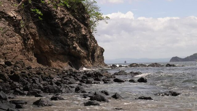 Ocean waves crashing on rocky shores of Playa Penca as fishing boat drives in background, Costa Rica