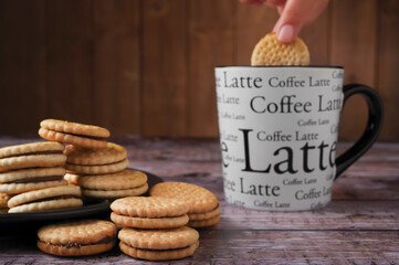 vanilla cookies with chocolate flavor filling , on a black plate, a steaming cup of coffee on a...