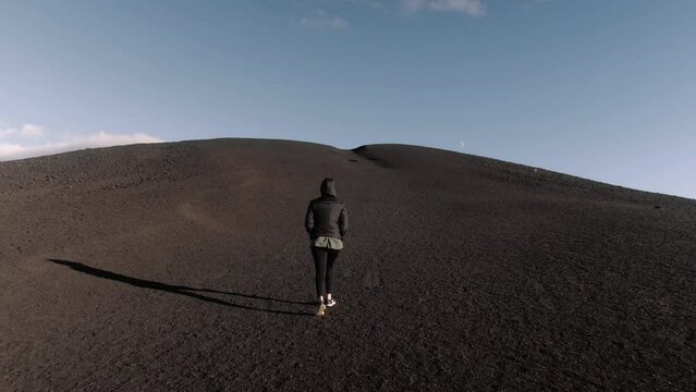 Wide gimbal shot of young petite woman walking up hill at craters of the moon in Idaho