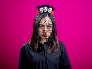 Portrait of an Asian Indonesian woman wearing a Halloween-themed costume, smiling, and looking quite spooky with her face covered by a mesh cloth. Isolated against a magenta background.