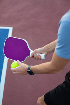 Close up abstract photo of a man holding a pickleball racket and a pickle ball ready to serve in on a pickleball court