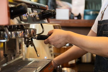 Close-up anonymous barista hands using professional coffee machine making hot espresso and pouring coffee to mug in cozy cafe, small businesses start up for young people lifestyle concept