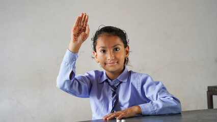 Happy Cute Indian, Asian Pretty elementary school child or kid in uniform raising hand in classroom. Education concept.