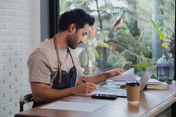 Attractive barista male or employee concentrate on stacks of tax declaration bills, restaurant...
