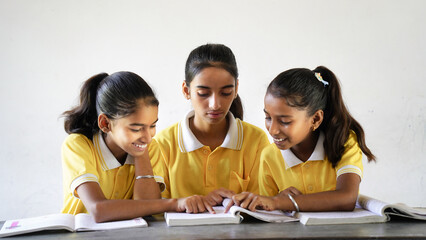 Indian schoolgirl sitting at desk in classroom, group of school kids with notebooks writing test,...