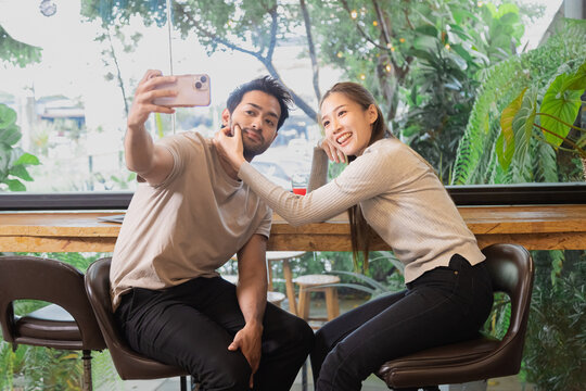 Happy couple enjoy taking selfie together in coffee shop. Beautiful Asian woman and Indian man meet at cafe to date together on anniversary. Lifestyle concept in love having date sit at restaurant