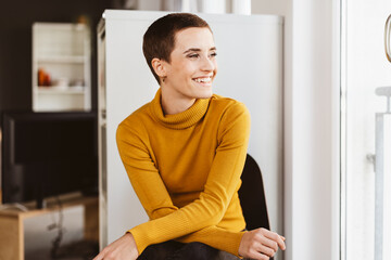 Fototapeta na wymiar Young Modern Woman with Short Hair Sits in Office Chair, Gazing Happily out of the Window