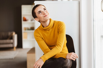 Young Modern Woman with Short Hair and Yellow Sweater Sitting in Office Chair, Smiling Upward