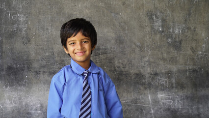 Cute Happy Indian school boy wearing uniform in the classroom near the chalk board