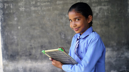 Rural School girl holding slate with English alphabet. Indian child writing A B C D alphabet on...