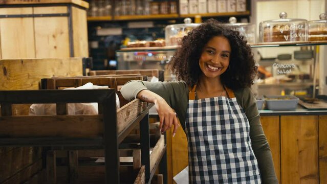 Portrait of smiling confident young woman wearing apron working in food shop or cafe - shot in slow motion